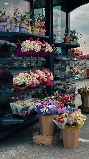 A display of various floral arrangements and bouquets at yeadingflorist.co.uk, situated on shelves inside a glass-walled shop or kiosk. The arrangement includes vibrant pink, white, purple, and yellow